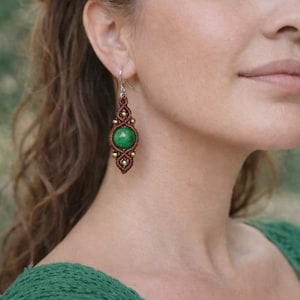 May include: Handmade macrame earrings featuring a vibrant green gemstone center. The earrings have a brown woven design with gold-colored beads. The hook is silver. The earrings are a bohemian style.