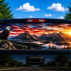 May include: A rear truck window decal featuring a bald eagle perched on a rock, a large American flag waving in the sky, and a scenic landscape of snow-capped mountains, a lake, and a vibrant sunset with orange and yellow light rays.