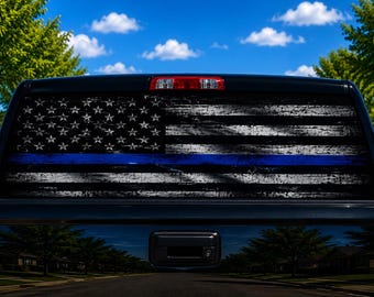 May include: A black truck rear window decal featuring a distressed American flag design in shades of black, white, and gray, with a single horizontal blue stripe running across the center of the flag, applied to the back window of a black pickup truck.