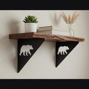 May include: A rustic wooden shelf with live edge detail, supported by black metal brackets featuring white bear silhouettes. The shelf holds a potted succulent, books, and decorative dried grasses. A stylish and functional home decor item.