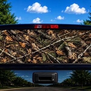 May include: A black pickup truck features a rear window decal with a detailed forest camouflage pattern. The design displays a realistic mix of brown oak leaves, tree bark textures, and thin white branches covering the entire glass surface.