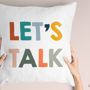 May include: White throw pillow with the text "LET'S TALK" in colorful, block letters. The letters are in shades of orange, teal, blue, yellow, pink, and green.