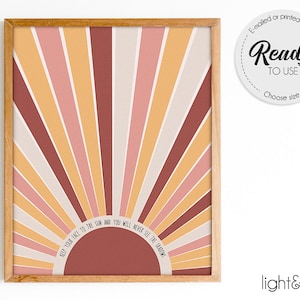 May include: A framed art print featuring a retro sunburst design in shades of pink, orange, and brown. The artwork includes the text "Keep your face to the sun and you will never see the shadows." The print is ready to use.