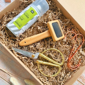 May include: A gift box filled with craft supplies, including a spray adhesive bottle labeled "Sprüh Kleber Spray Glue Colle en Aerosol 150 ml", a wooden brush, gold scissors, and copper wire.