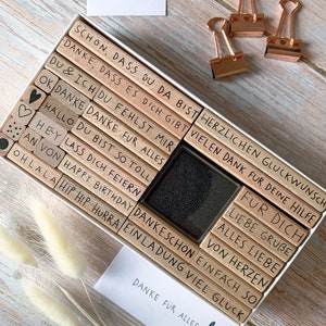 May include: A set of wooden stamps in a white box with a black ink pad. The stamps have German phrases like "Danke f&uuml;r alles" and "F&uuml;r dich".