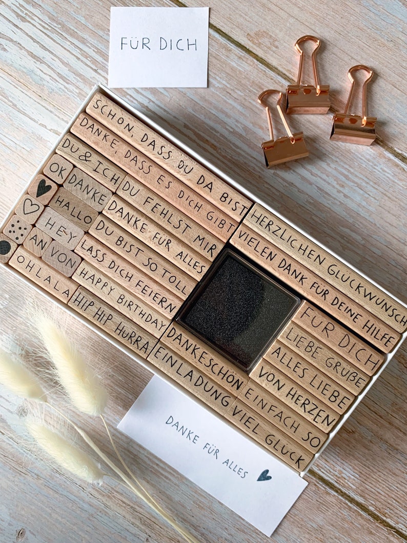 May include: A set of wooden stamps in a white box with a black ink pad. The stamps have German phrases like "Danke f&uuml;r alles" and "F&uuml;r dich".