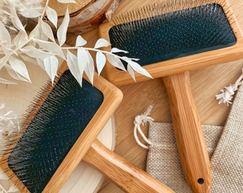 May include: Two wooden pet grooming brushes with black bristles and wooden handles. The brushes are on a wooden surface with a burlap bag and dried flowers.