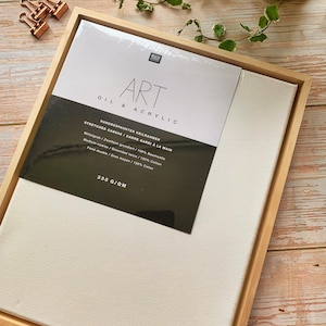 Op de afbeelding: Een houten frame met een wit canvas dat er in gespannen is. Het canvas is gelabeld "Art Olie & Acryl" en heeft de tekst "Handbespannter Keilrahmen Stretched Canvas/Cadre Garni a la Main Mittelgrob/Zweifach grundiert/100% Baumwolle Medium-coarse / Grounded twice/100% Cotton Fond double/Gres moyen/100% Caton 330 G/QM".