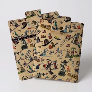 May include: Beige fabric pouches with a medieval-themed print featuring snails, figures, and foliage. The pouches have a flap closure with a snap. The fabric has a vintage, parchment-like appearance.
