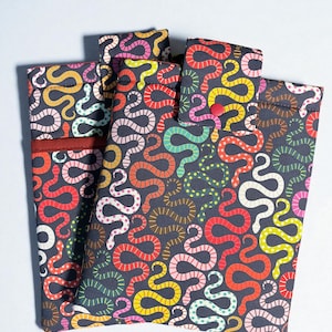 May include: Several fabric cases with a repeating pattern of colorful snakes in red, yellow, pink, and green on a dark gray background. The cases are rectangular and appear to be closed with a button or flap.