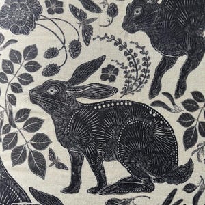 Pode incluir: Ilustra&ccedil;&atilde;o em preto e branco de coelhos e desenhos florais sobre um fundo creme. Os coelhos s&atilde;o representados de forma estilizada, quase geom&eacute;trica, com detalhes intrincados. Os desenhos florais incluem rosas, folhas e outros elementos bot&acirc;nicos.