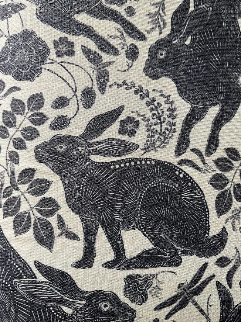 Pode incluir: Ilustra&ccedil;&atilde;o em preto e branco de coelhos e desenhos florais sobre um fundo creme. Os coelhos s&atilde;o representados de forma estilizada, quase geom&eacute;trica, com detalhes intrincados. Os desenhos florais incluem rosas, folhas e outros elementos bot&acirc;nicos.