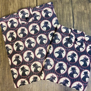 Könnte beinhalten: Zwei schwarze und weiße Stoffbeutel mit einem sich wiederholenden Muster von Pestärzten, die Schnabelmasken tragen. Die Beutel haben einen schwarzen Knopfverschluss.