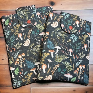 Può includere: Tre pochette in tessuto con sfondo verde scuro e un motivo di funghi, felci e altre foglie. Le pochette hanno una chiusura a lembo con un bottone rosso.