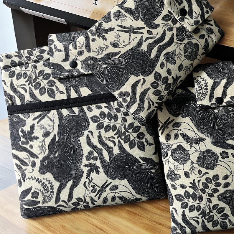 Pode incluir: Tr&ecirc;s capas para laptop de tecido preto e branco com um padr&atilde;o repetido de lebres, flores e folhas. As capas s&atilde;o feitas de tecido de linho natural.