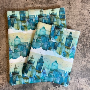 May include: Two fabric pouches with a blue and green watercolour cityscape design. The smaller pouch has a blue snap closure.