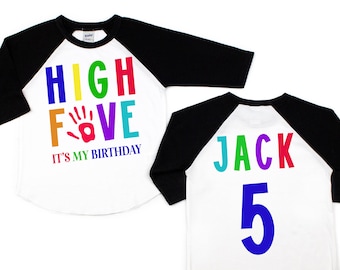 May include: A white and black baseball style shirt with rainbow colored text that says "HIGH FIVE" and a red handprint. The text below the rainbow text says "IT'S MY BIRTHDAY". The back of the shirt has the name "JACK" in rainbow colors and the number "5" in blue.