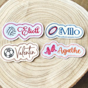 Peut inclure: Quatre écussons brodés avec des motifs sportifs et des noms tels que "Eliott" avec un ballon de volley-ball, "Milo" avec un ballon de rugby, "Valentin" avec un ballon de foot et "Agathe" avec des chaussons de danse.