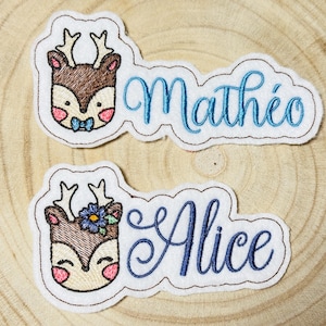 Może przedstawiać: Dwa białe filcowe łatki z haftowanymi twarzami jeleni i nazwami. Górna łatka ma haftowane niebieskie imię "Mathéo", a dolna łatka ma haftowane niebieskie imię "Alice".