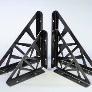 May include: Four black metal shelf brackets with a geometric design. The brackets are triangular in shape and have a decorative pattern of intersecting lines.