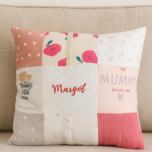 以下が含まれることがあります： ピンク、白、グレーなど様々な生地と色を使ったパッチワーククッション。赤い文字で「Margot」という名前が刺繍されており、「Daddy's little one」と「my mummy loves me」というフレーズも含まれています。