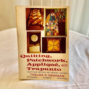 Pode incluir: Um livro intitulado "Quilting, Patchwork, Appliqué, and Trapunto" de Thelma R. Newman. A capa do livro apresenta quatro imagens coloridas de colchas e um travesseiro. O livro inclui 400 fotografias, 30 diagramas e 26 placas coloridas.