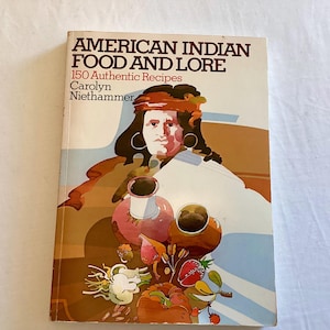 May include: A book cover with a colorful illustration of a Native American woman wearing a red headband and holding a bowl. The title of the book is "American Indian Food and Lore" with the subtitle "150 Authentic Recipes" and the author's name "Carolyn Niethammer".