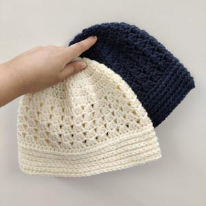 May include: Two crocheted hats, one white and one navy blue. The white hat is on top of the navy blue hat.