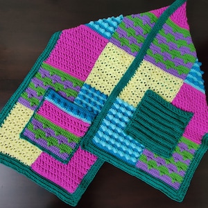 May include: A crocheted blanket with a patchwork design featuring various colours and textures, including pink, green, blue, and yellow.