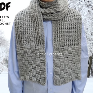 May include: A gray crocheted scarf with a woven pattern. The scarf is worn by a person wearing a light blue button-down shirt. "Let's all crochet" is written on the scarf.