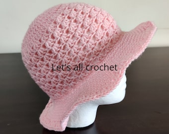 May include: A pink crocheted sun hat with a wide brim. The hat is made with a delicate stitch pattern and has a scalloped edge.