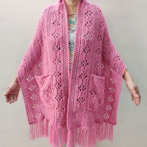 May include: A pink crocheted shawl with two pockets and fringe trim.