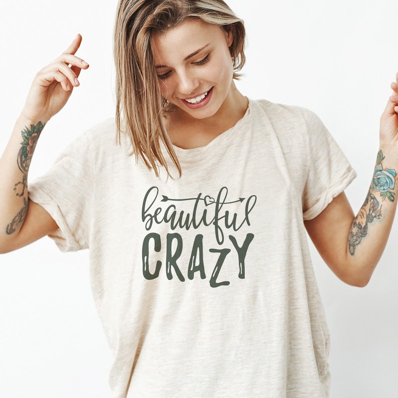 May include: A beige t-shirt with the text "beautiful crazy" in dark green lettering with an arrow and a heart above the word "beautiful".