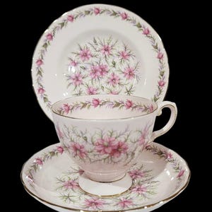 May include: A vintage tea set featuring a teacup, saucer, and a small plate. The set has a white background with a pink floral pattern and gold trim. The teacup is approximately 3 inches tall.