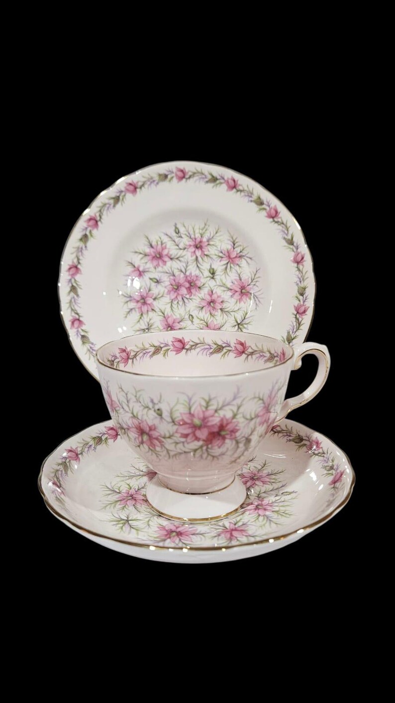 May include: A vintage tea set featuring a teacup, saucer, and a small plate. The set has a white background with a pink floral pattern and gold trim. The teacup is approximately 3 inches tall.