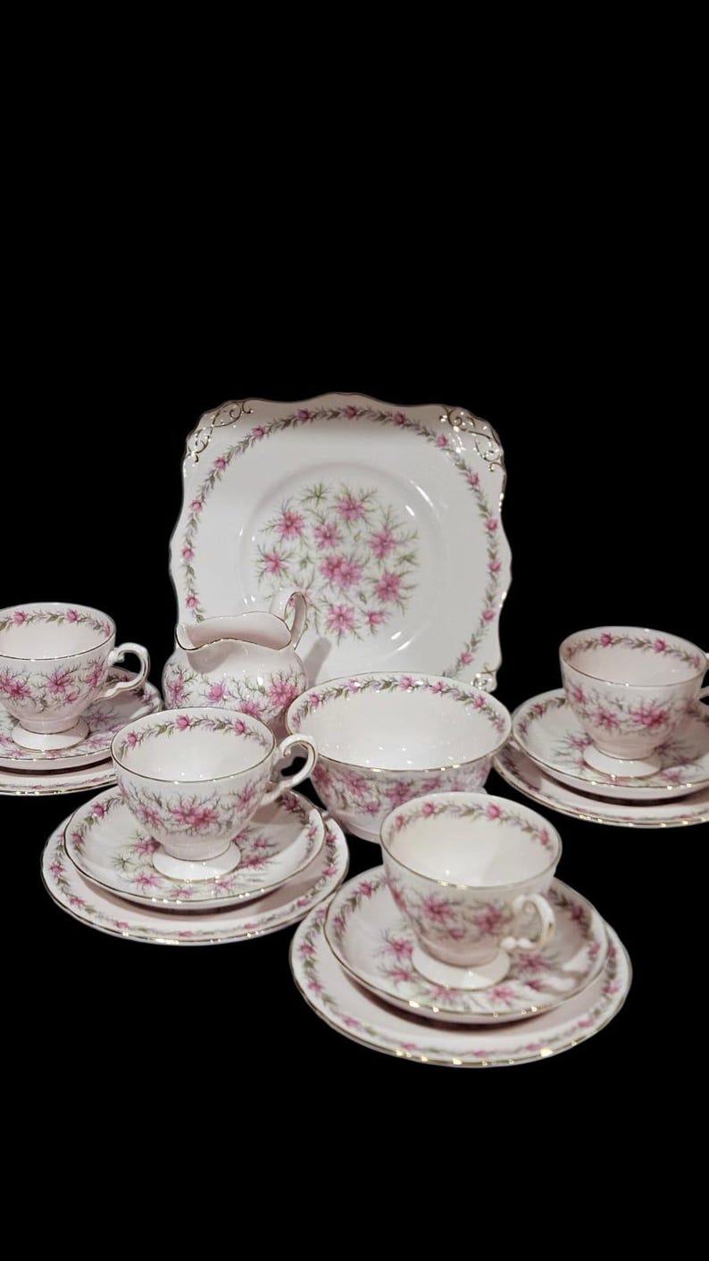 May include: A vintage tea set with a floral pattern. The set includes teacups, saucers, a sugar bowl, a serving bowl, and a cake plate. The pieces are white with pink floral designs and gold trim. A classic tea party set.