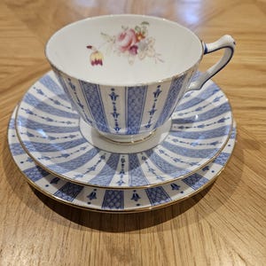May include: A blue and white teacup and saucer set with a floral design. The cup and saucer have a gold trim.