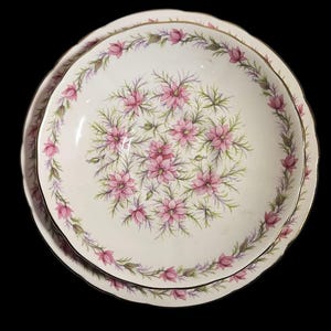 May include: Two white ceramic plates with a floral design. The plates feature a pink floral pattern in the center and around the rim, with a gold trim. The plates are set against a black background.