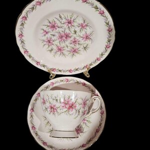 May include: A vintage tea set featuring a teacup, saucer, and plate. The white porcelain pieces are adorned with a pink floral pattern and gold trim. The floral design is repeated on each piece, creating a cohesive and elegant look.