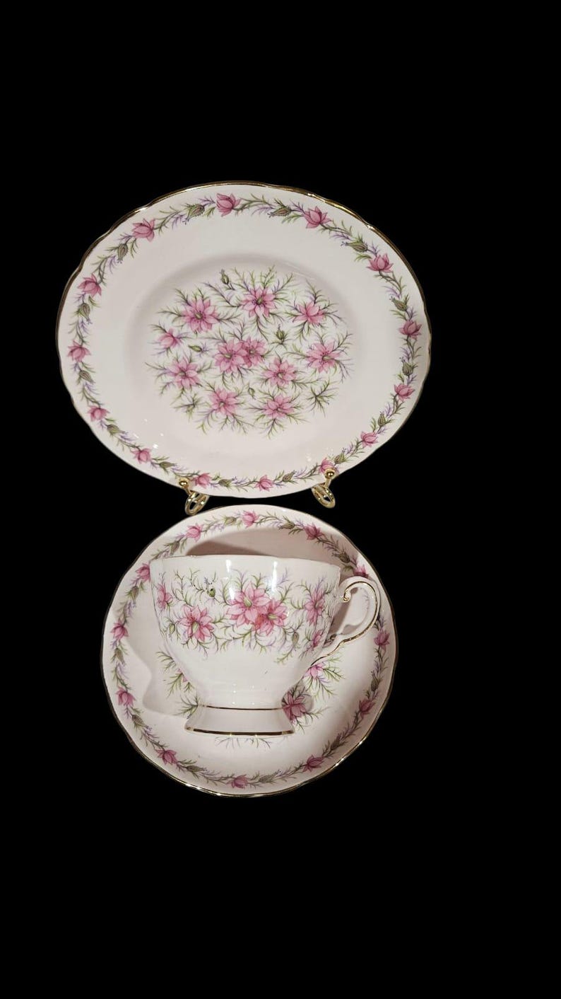 May include: A vintage tea set featuring a teacup, saucer, and plate. The white porcelain pieces are adorned with a pink floral pattern and gold trim. The floral design is repeated on each piece, creating a cohesive and elegant look.