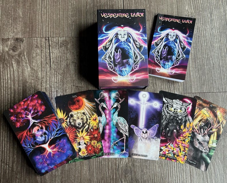May include: A tarot deck with a black background and colorful illustrations. The box features a woman with flowing hair and a glowing orb. The cards depict various scenes with animals, plants, and mystical symbols. The deck is called "Vespertine Tarot".