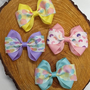 May include: Four handmade hair bows with different patterns. The bows are made of ribbon and are tied in a knot. The patterns include pastel jelly beans, feathers, and polka dots.