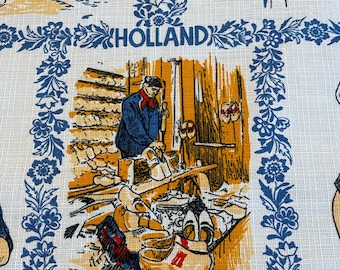 May include: A vintage fabric featuring illustrations of Dutch scenes, including buildings, a shoemaker's workshop, and the word "HOLLAND" in blue lettering. The fabric has a white background with blue floral borders.