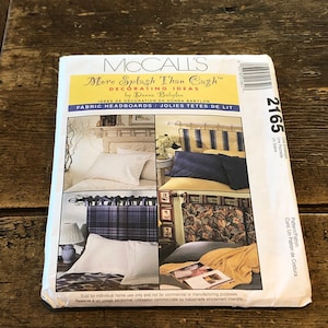 May include: A McCall's sewing pattern for fabric headboards. The pattern is for two different styles of headboards, one with a plaid fabric and one with a striped fabric. The pattern is called "More Splash Than Cash" and is by Donna Babylon.