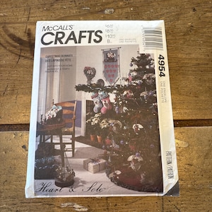 Puede incluir: Un sobre de patrón de costura vintage de McCall's Crafts que presenta un árbol de Navidad decorado con adornos hechos a mano, una media y una pancarta. El patrón se titula "Christmas Bunnies... Des Lapins de Fete..." y el número de patrón es 4954.