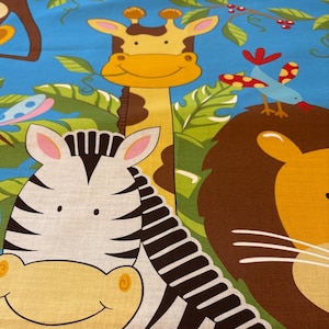 May include: A colorful fabric with a blue background featuring a smiling zebra, a giraffe, a lion, a mouse, and a monkey. The fabric also has green leaves and red berries.