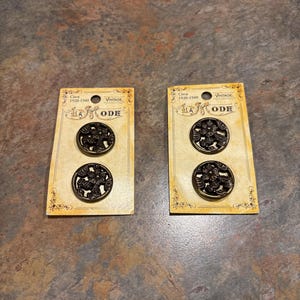 May include: Two vintage button cards, each with two dark bronze-colored buttons. The buttons have a floral design. The cards are labeled "LA MODE" and "VINTAGE" with the text "Circa 1920-1940".