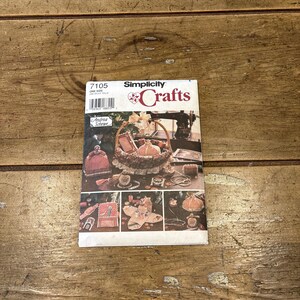 May include: A vintage Simplicity Crafts pattern booklet, featuring a variety of craft projects. The cover displays a basket, hats, and other handmade items. The booklet is labeled "7105" and includes the name "Andrea Schewe".