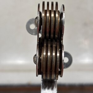 May include: A kitchen tool featuring two stacked sets of four circular metal blades arranged in parallel rows. The silver-toned blades are held together by a central metal frame and are attached to a light-colored handle at the base of the unit.