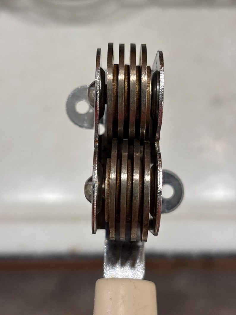 May include: A kitchen tool featuring two stacked sets of four circular metal blades arranged in parallel rows. The silver-toned blades are held together by a central metal frame and are attached to a light-colored handle at the base of the unit.